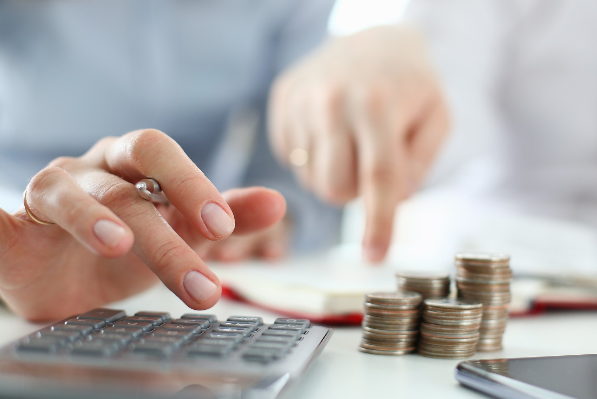 Na imagem temos um casal, cuidando de sua finanças fazendo conta na calculadora. No canto inferior direito uma pilha de moedas. Na imagem temos um casal, cuidando de sua finanças fazendo conta na calculadora. No canto inferior direito uma pilha de moedas.