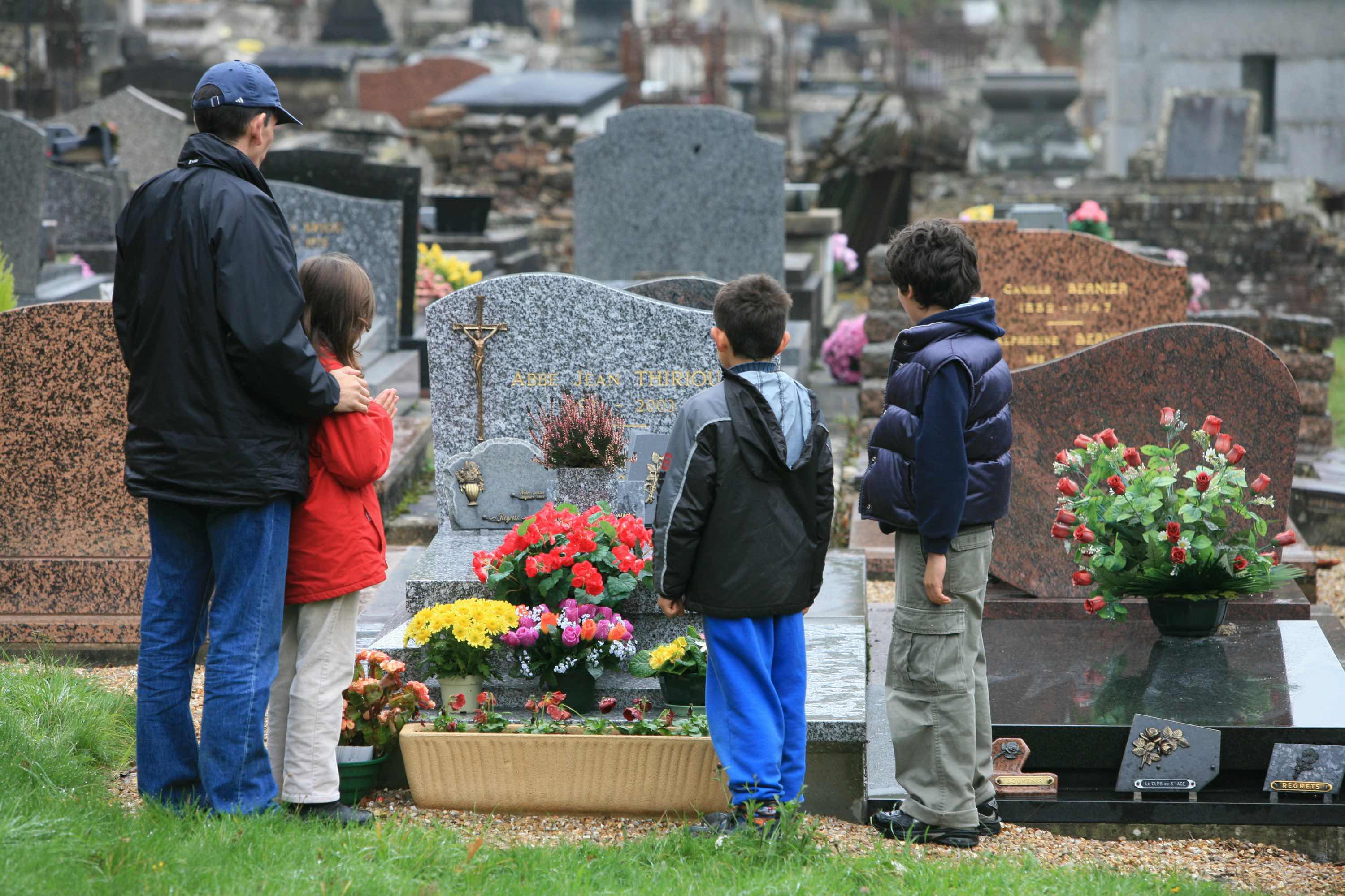 Três crianças e um adulto em volta de uma sepultura.